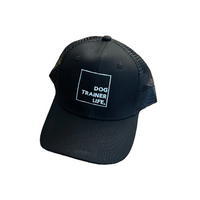 Black cap with 'Dog Trainer Life' text on a wooden table