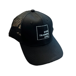 Black cap with 'Dog Trainer Life' text on a wooden floor